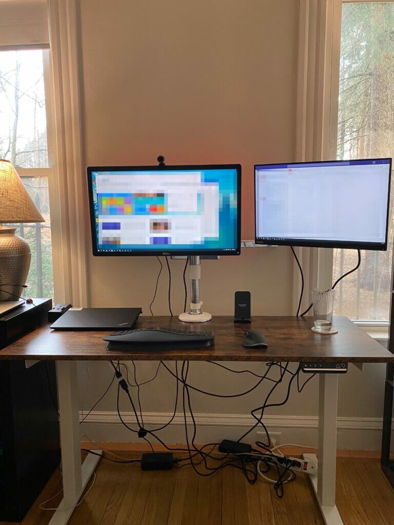 Office desk with wires everywhere from a computer, wires, and two monitors 